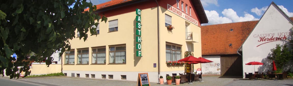 Außenansicht des Gasthof Hotel Herderich mit Terrasse und roten Sonnenschirmen